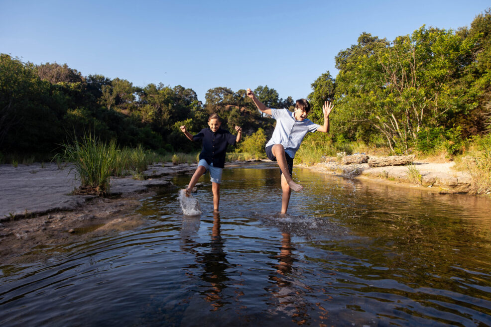 two brothers splashing around during their family photo session in austin, texas at bull creek park